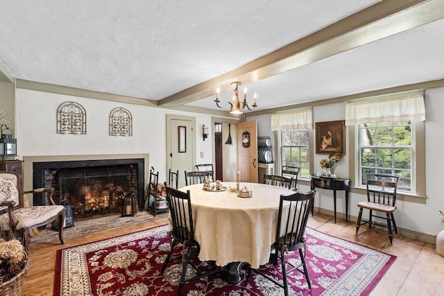 dining space with wood finished floors, beam ceiling, a chandelier, baseboards, and a lit fireplace