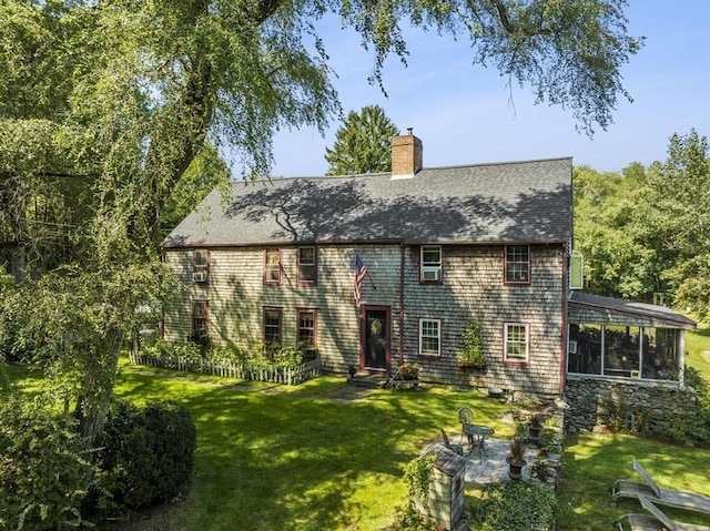 rear view of house featuring a sunroom, a chimney, a lawn, and roof with shingles