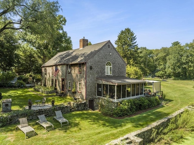 back of property with a sunroom, a chimney, a yard, and a shingled roof