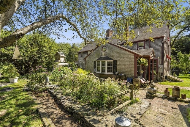 view of side of home featuring a chimney, a patio area, and roof with shingles