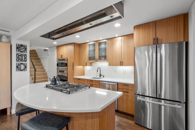 kitchen with a kitchen island, glass insert cabinets, stainless steel appliances, light countertops, and a sink