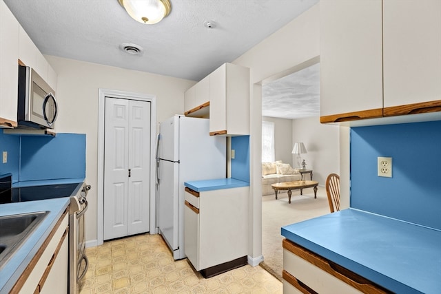 kitchen featuring white cabinetry, sink, light colored carpet, appliances with stainless steel finishes, and a textured ceiling