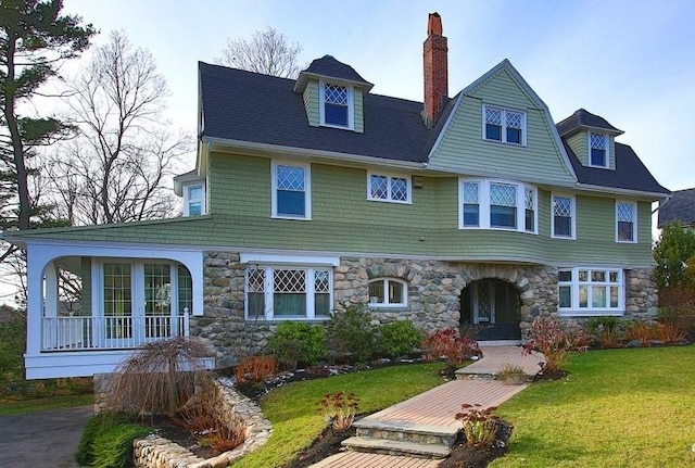 view of front of property with stone siding, a front yard, and a chimney