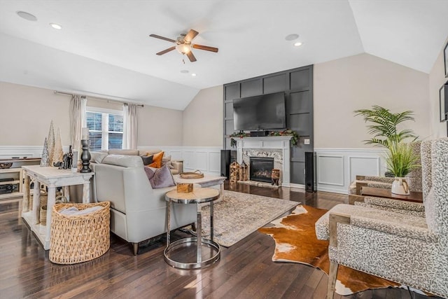 living area with ceiling fan, a glass covered fireplace, dark wood-style flooring, and vaulted ceiling