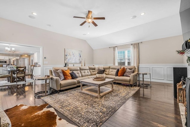 living room featuring ceiling fan with notable chandelier, dark wood finished floors, wainscoting, and vaulted ceiling