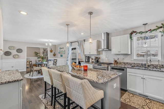 kitchen with a sink, stainless steel appliances, a breakfast bar area, and wall chimney range hood