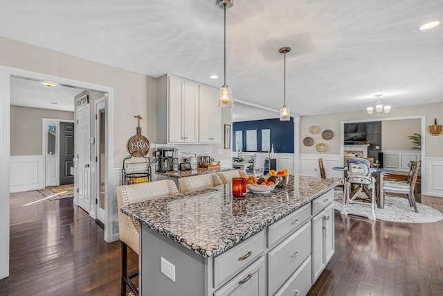 kitchen featuring light stone counters, a kitchen breakfast bar, pendant lighting, and dark wood-style flooring