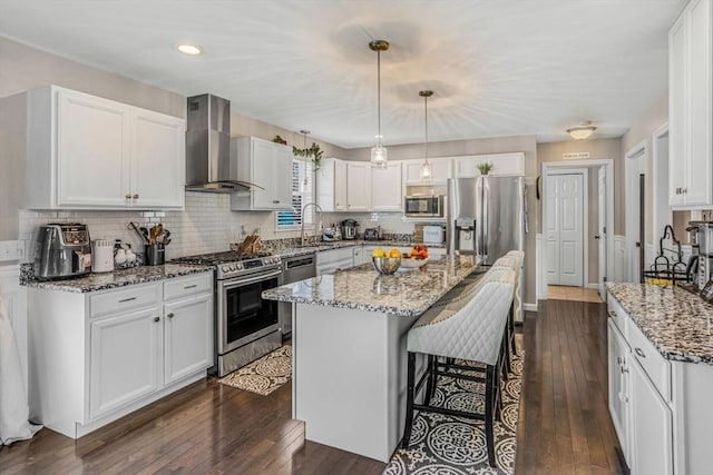 kitchen with light stone countertops, a breakfast bar, stainless steel appliances, dark wood-type flooring, and wall chimney exhaust hood