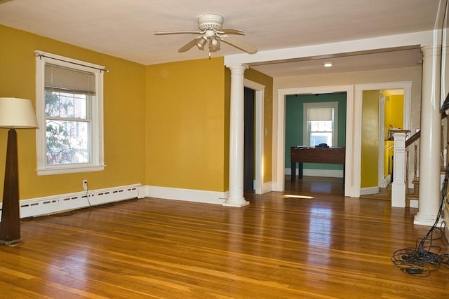 unfurnished room featuring a baseboard heating unit, a healthy amount of sunlight, ornate columns, and wood finished floors