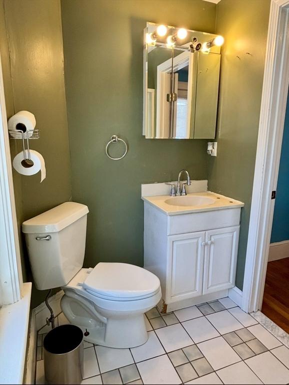 half bathroom featuring toilet, tile patterned flooring, baseboards, and vanity