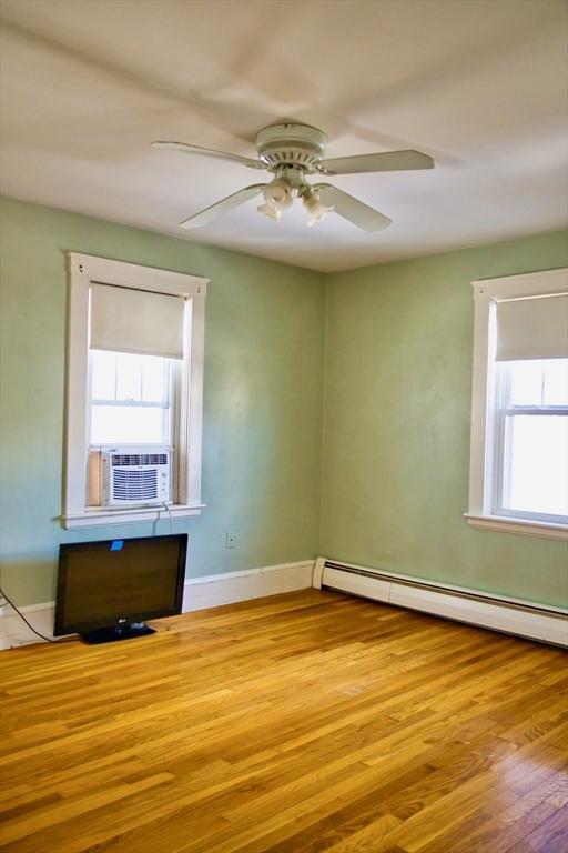 spare room featuring cooling unit, wood finished floors, baseboards, and a baseboard radiator