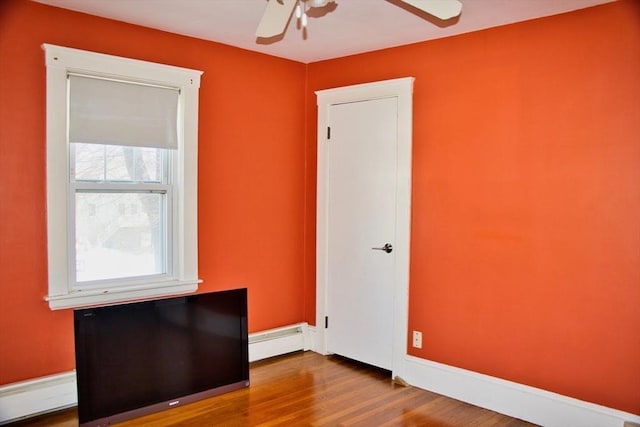 unfurnished room with a baseboard heating unit, wood finished floors, baseboards, and a ceiling fan