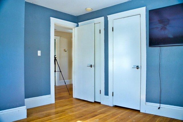 unfurnished bedroom featuring two closets, baseboards, and wood finished floors