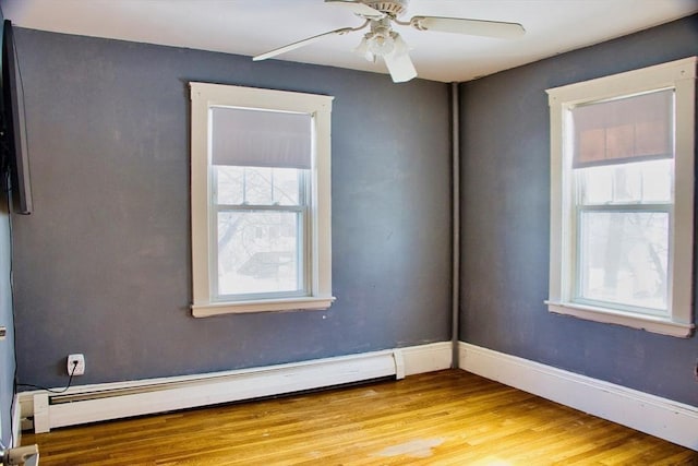 spare room featuring ceiling fan, baseboard heating, light wood-type flooring, and baseboards