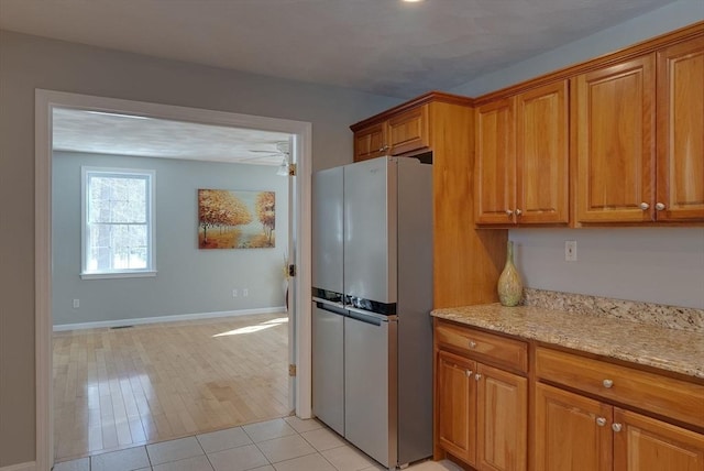 kitchen featuring light stone countertops, baseboards, brown cabinets, and freestanding refrigerator