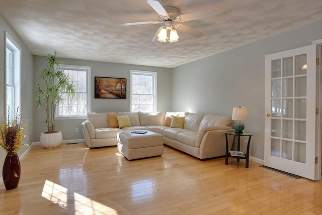 living room with a ceiling fan, light wood-type flooring, a wealth of natural light, and baseboards