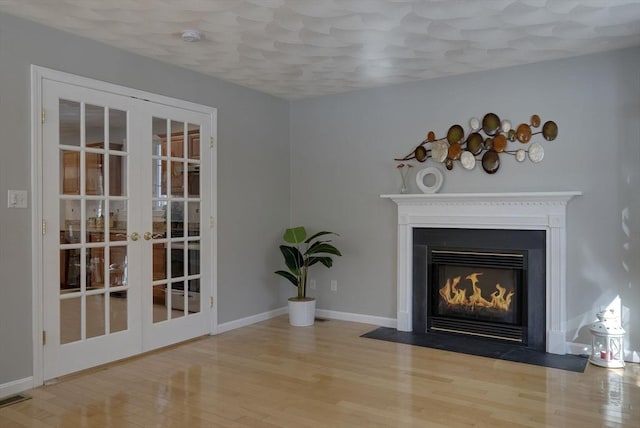 interior details with visible vents, baseboards, a fireplace with flush hearth, wood finished floors, and french doors