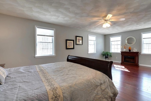 bedroom with dark wood-style floors, a fireplace, baseboards, and ceiling fan