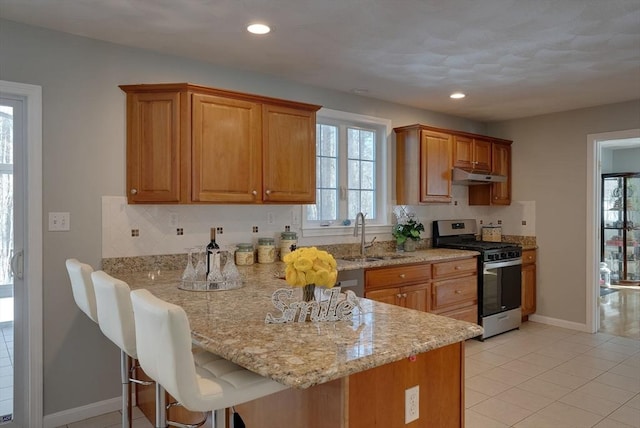 kitchen with stainless steel range with gas cooktop, a sink, a peninsula, under cabinet range hood, and a kitchen breakfast bar