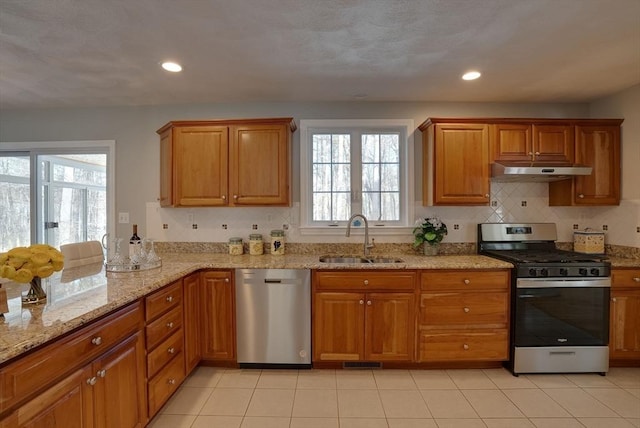 kitchen featuring appliances with stainless steel finishes, brown cabinetry, a sink, and under cabinet range hood