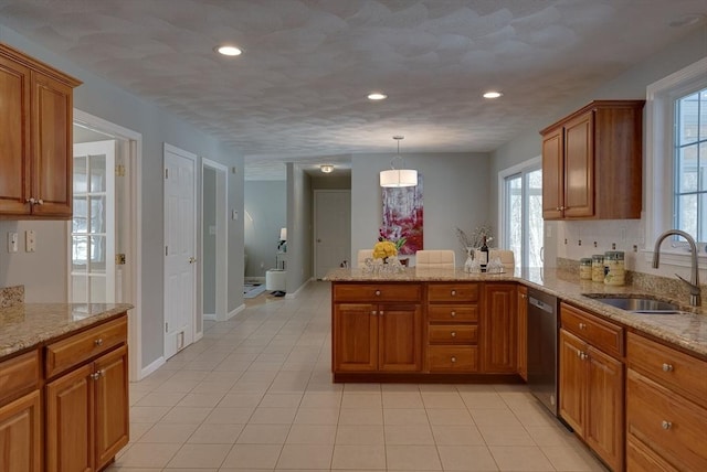 kitchen featuring a peninsula, stainless steel dishwasher, brown cabinetry, and a sink