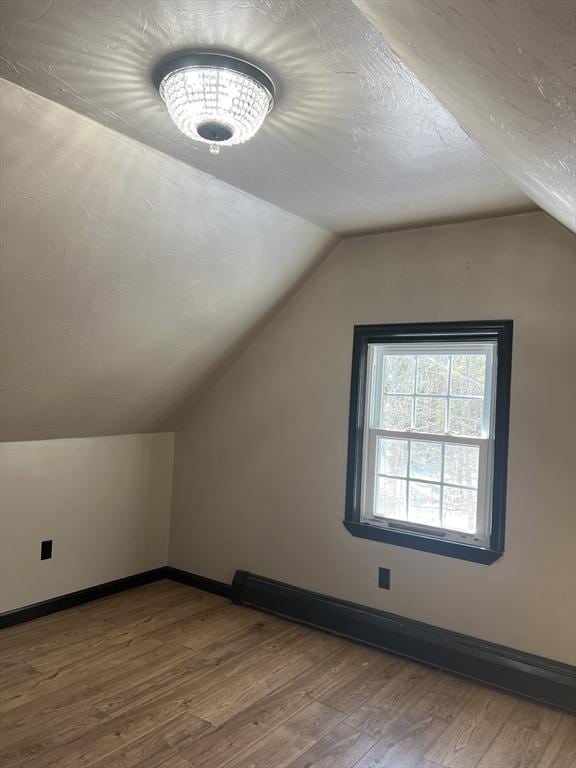 bonus room featuring baseboard heating, lofted ceiling, hardwood / wood-style floors, and a textured ceiling