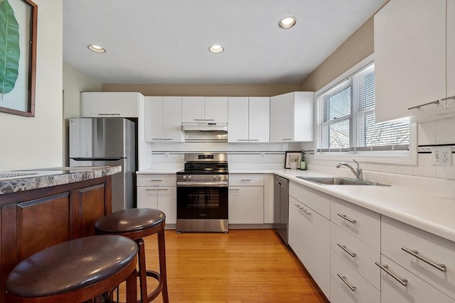 kitchen featuring light wood-style flooring, a sink, under cabinet range hood, appliances with stainless steel finishes, and decorative backsplash