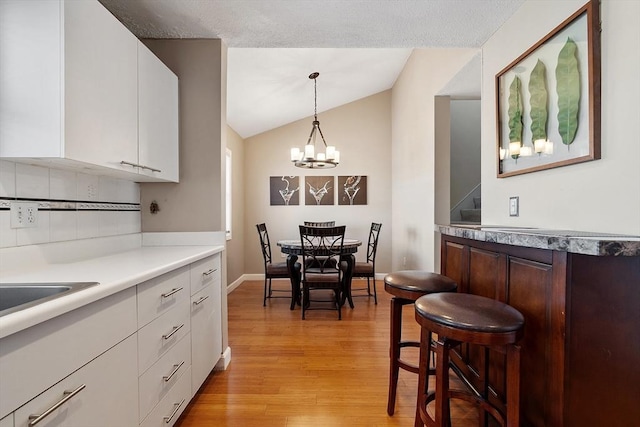 dining room featuring stairway, baseboards, lofted ceiling, light wood-type flooring, and a chandelier