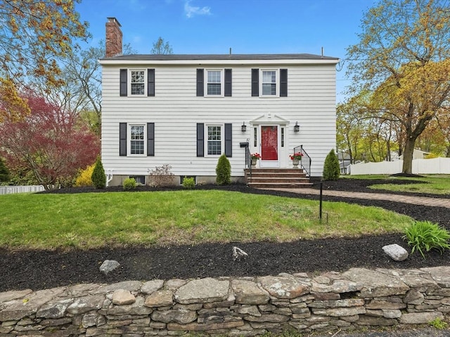colonial-style house featuring fence, a chimney, and a front yard