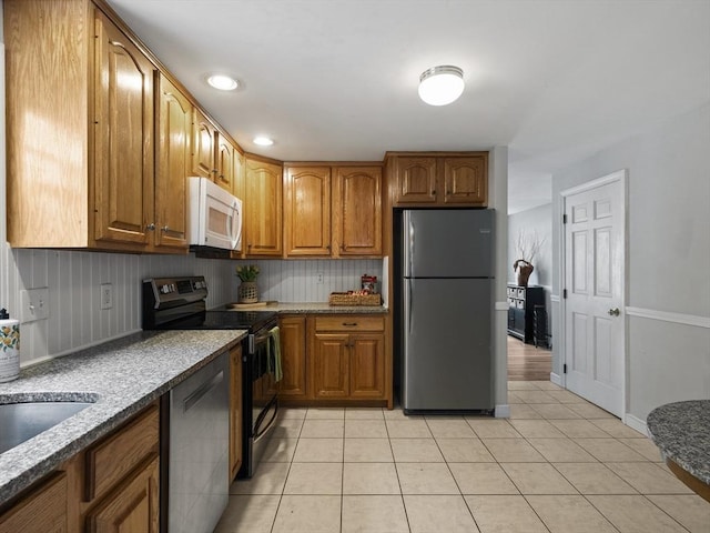 kitchen featuring brown cabinetry, stainless steel appliances, recessed lighting, stone counters, and light tile patterned floors
