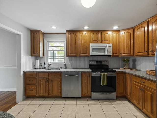 kitchen featuring stainless steel appliances, stone countertops, brown cabinetry, and a sink
