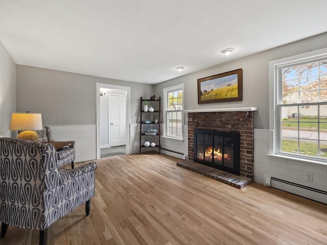 living area with a fireplace, plenty of natural light, wood finished floors, and a baseboard radiator