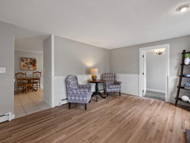 sitting room featuring a baseboard heating unit, wood finished floors, and a wainscoted wall