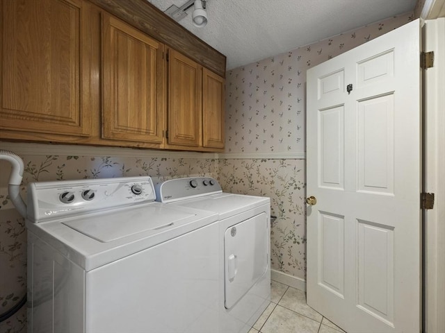 clothes washing area with a textured ceiling, cabinet space, light tile patterned floors, wallpapered walls, and washer and clothes dryer