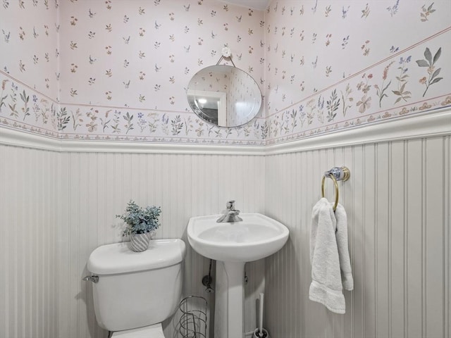 bathroom with wainscoting, toilet, and wallpapered walls