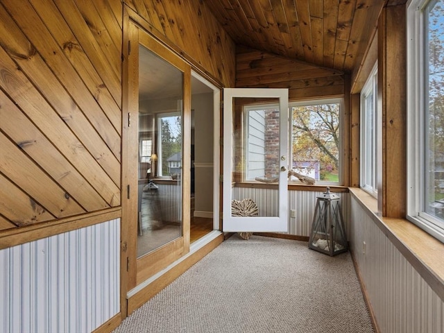 unfurnished sunroom featuring carpet flooring, lofted ceiling, wooden walls, and wooden ceiling