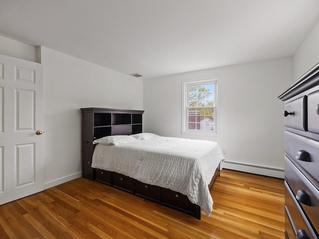 bedroom with a baseboard heating unit, wood finished floors, and visible vents
