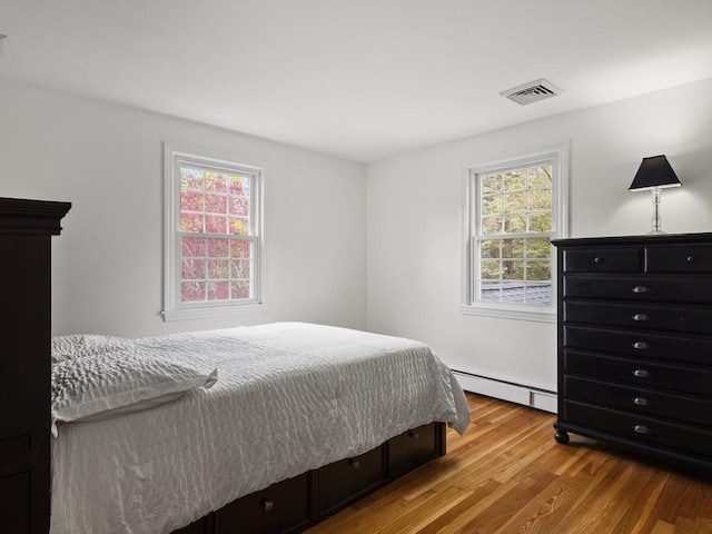 bedroom featuring visible vents, a baseboard heating unit, and wood finished floors