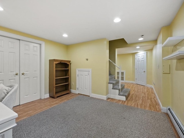 finished below grade area with stairs, recessed lighting, wood finished floors, and a baseboard radiator
