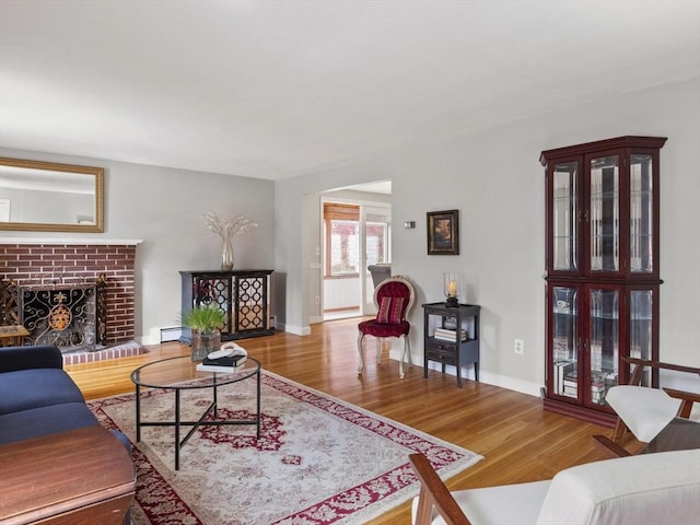 living area featuring baseboard heating, baseboards, wood finished floors, and a fireplace