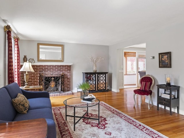 living room with baseboards, a brick fireplace, and wood finished floors