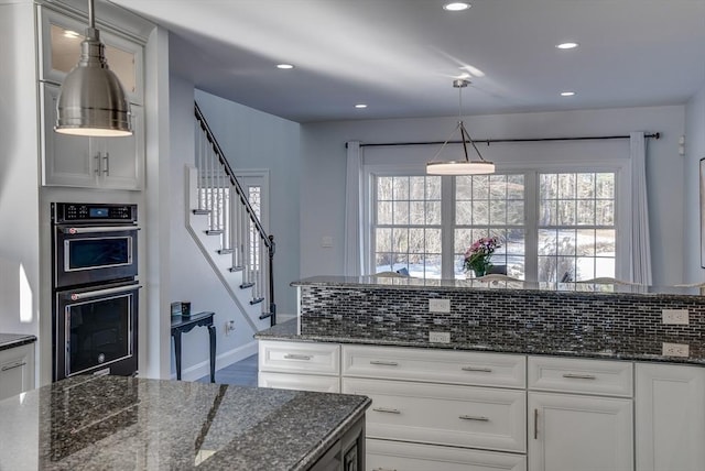 kitchen featuring white cabinetry, double oven, hanging light fixtures, and dark stone counters