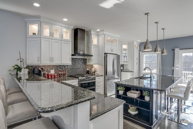 kitchen with wall chimney exhaust hood, a kitchen bar, sink, appliances with stainless steel finishes, and dark stone counters