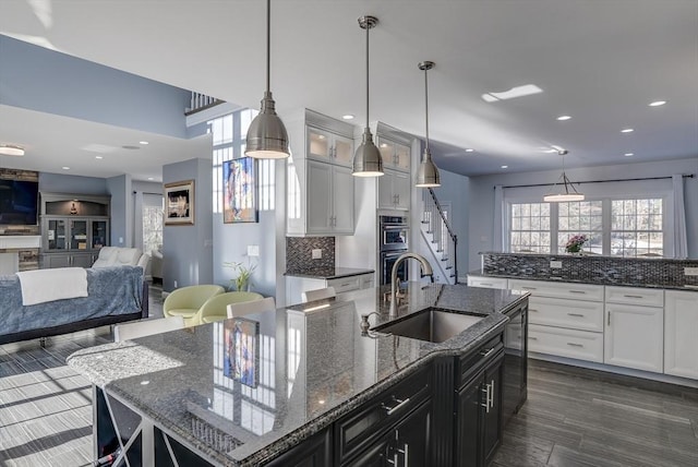 kitchen featuring white cabinetry, a kitchen island with sink, sink, and hanging light fixtures