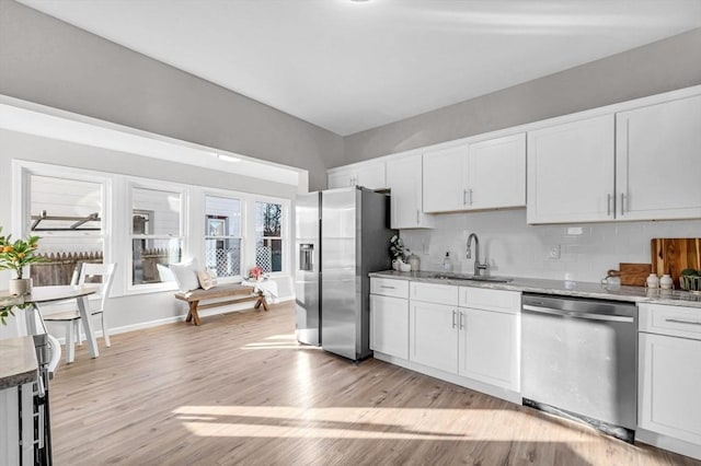 kitchen with sink, light hardwood / wood-style flooring, appliances with stainless steel finishes, light stone counters, and white cabinetry