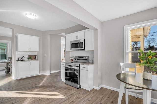 kitchen with stainless steel appliances, tasteful backsplash, light stone counters, white cabinets, and light wood-type flooring