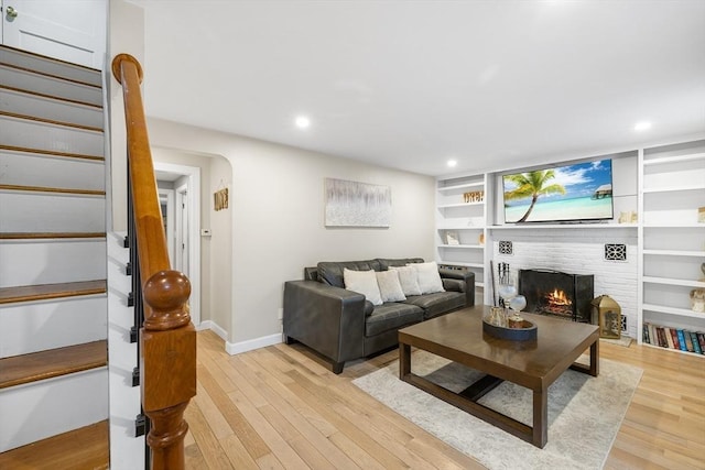 living area with built in shelves, light wood-style flooring, baseboards, a brick fireplace, and stairs