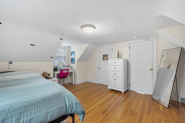 bedroom with baseboards, lofted ceiling, visible vents, and light wood finished floors