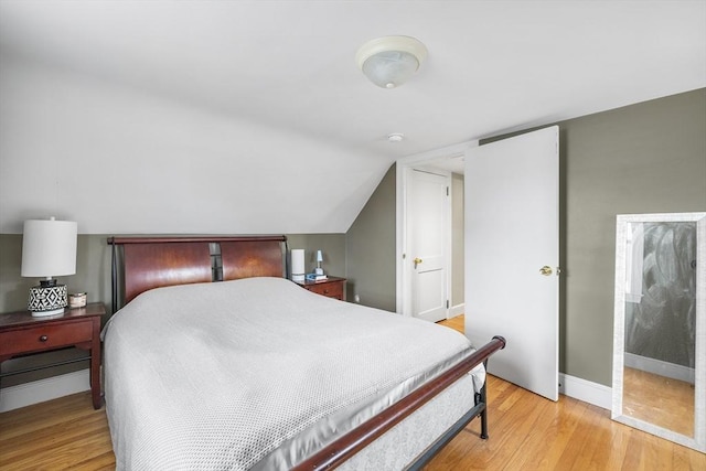 bedroom with light wood-type flooring, baseboards, and vaulted ceiling