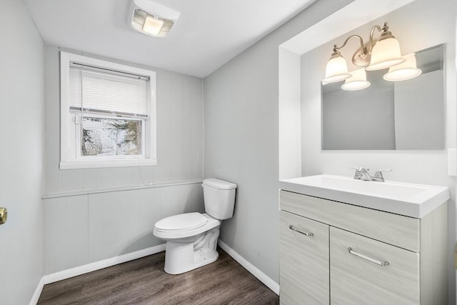 half bathroom featuring vanity, toilet, wood finished floors, and baseboards